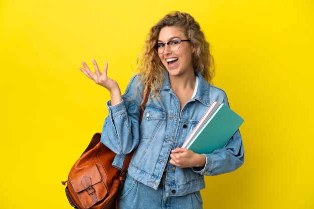 Giovane studentessa caucasica isolata su sfondo giallo che estende le mani di lato per invitare a venire