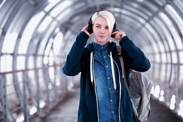 Giovane studentessa che ascolta musica in grandi cuffie nel tunnel della metropolitana