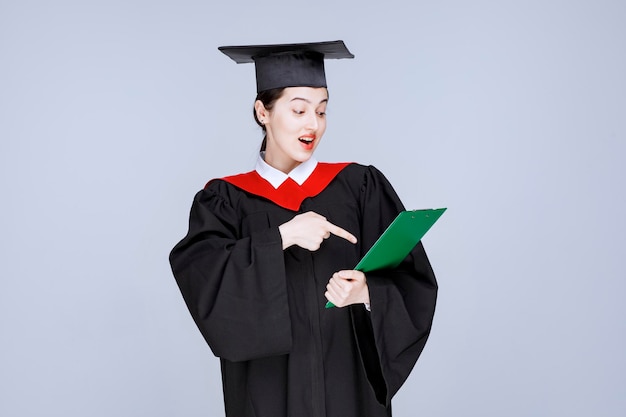 Giovane studentessa laureata che indica al diploma. Foto di alta qualità