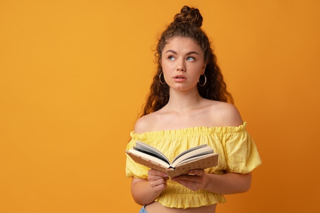 Giovane studentessa riccia che tiene libro su sfondo giallo yellow