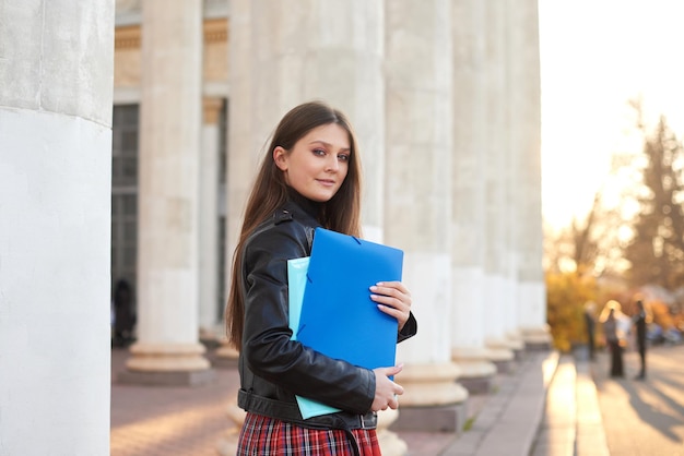 Giovane studentessa sorridente contro l'università Donna carina tiene in mano cartelle e quaderni