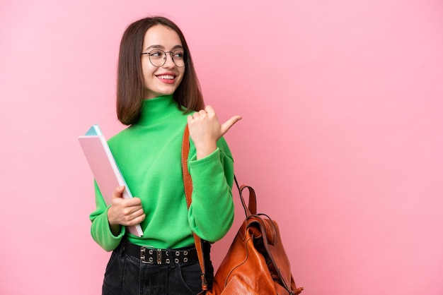 Giovane studentessa ucraina isolata su sfondo rosa che indica il lato per presentare un prodotto