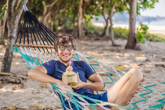 Giovane sulla spiaggia in un'amaca con un drink