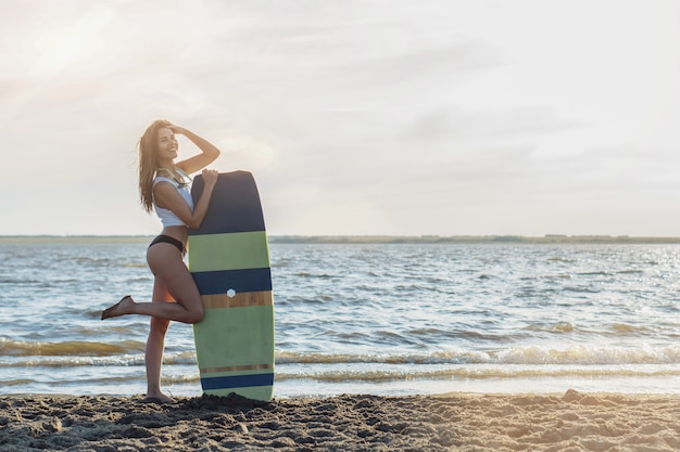 Giovane surfista in posa con la sua tavola da surf sulla spiaggia