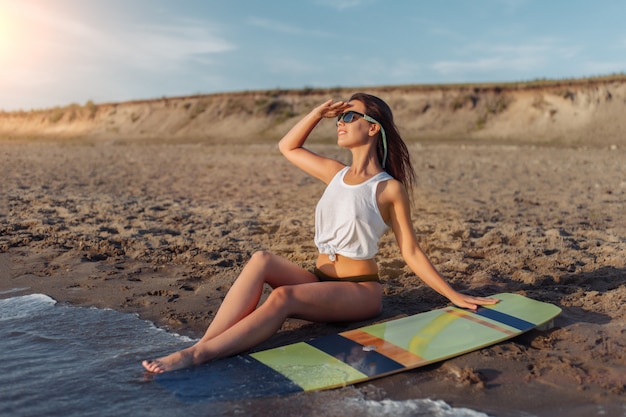 Giovane surfista in posa con la sua tavola da surf sulla spiaggia