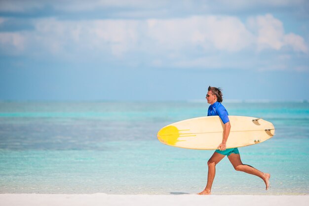 Giovane surfista in spiaggia bianca con tavola da surf gialla