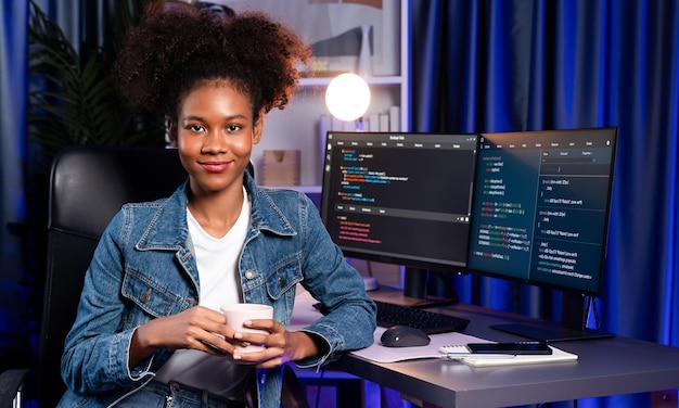 Giovane sviluppatore IT africano che indossa una camicia jeans che presenta un programma su schermi di computer che visualizza dati codificati di applicazioni e siti web creando una versione innovativa e aggiornata del software Tastemaker