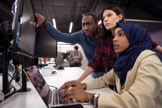 giovane team aziendale multietnico di sviluppatori di software che lavorano insieme utilizzando un computer portatile durante la scrittura del codice di programmazione nel moderno ufficio di avvio
