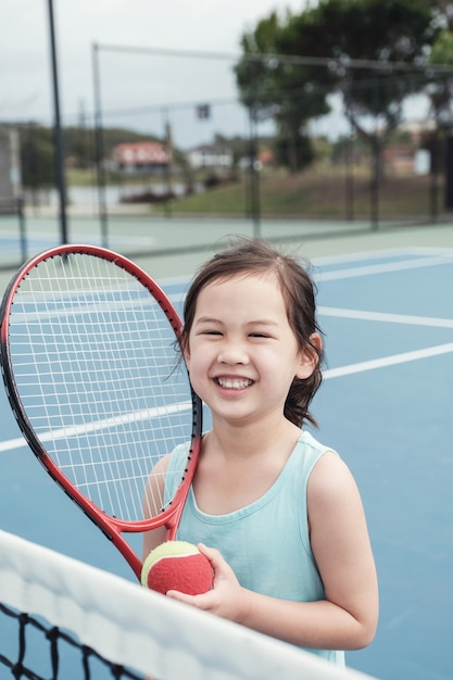 Giovane tennista asiatico della ragazza sulla corte blu all&#39;aperto