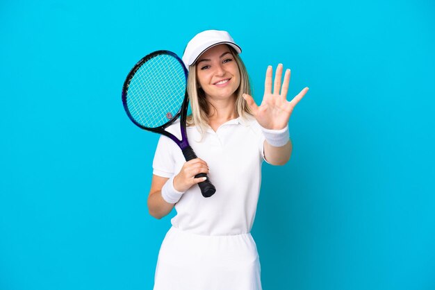 Giovane tennista donna rumena isolata su sfondo blu contando cinque con le dita