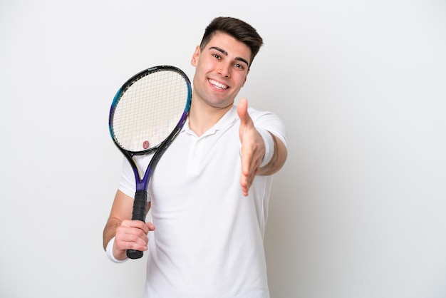 Giovane tennista uomo isolato su sfondo bianco che stringe la mano per la chiusura di un buon affare