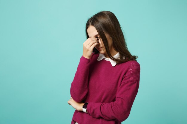 Giovane triste sconvolto perplesso disturbare bruna donna ragazza tenendo gli occhi chiusi, mettendo la mano sul naso in posa isolato su sfondo blu parete ritratto in studio. Concetto di stile di vita delle persone. Mock up spazio di copia.