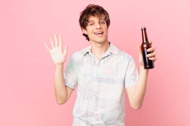 Giovane turista con una birra sorridente felicemente agitando la mano accogliendoti e salutandoti