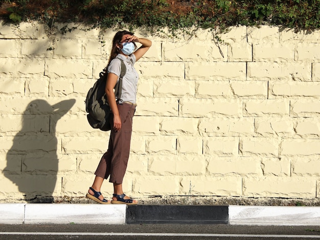 Giovane turista in maschera facciale si trova sul lato della strada e si copre gli occhi dal sole