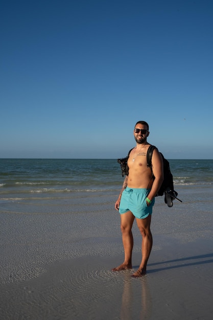 Giovane turista maschio che passeggia lungo la spiaggia di Holbox con un costume da bagno e una macchina fotografica