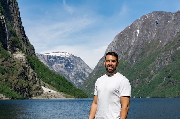 Giovane turista maschio in primo piano e dietro di lui le alte montagne e il fiordo di Gudvangen in Norvegia