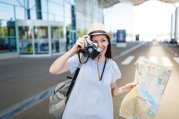 Giovane turista viaggiatrice scatta foto con una macchina fotografica vintage retrò, tiene una mappa cartacea all'aeroporto internazionale