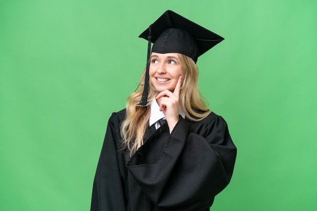 Giovane università inglese donna laureata su sfondo isolato pensando un'idea mentre guardando in alto