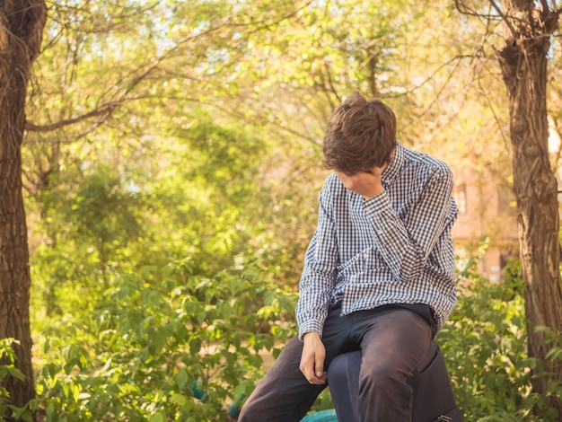 Giovane uomo adolescente stanco che si siede sulla grande borsa della borsa dei bagagli all&#39;aperto nella via della città di estate