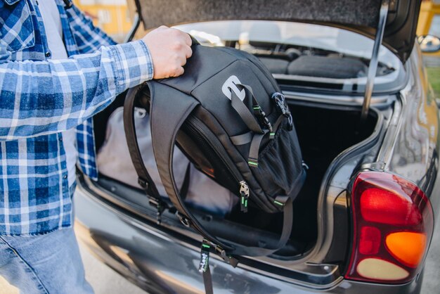 Giovane uomo adulto che mette la borsa nel bagagliaio dell'auto concetto di viaggio in auto