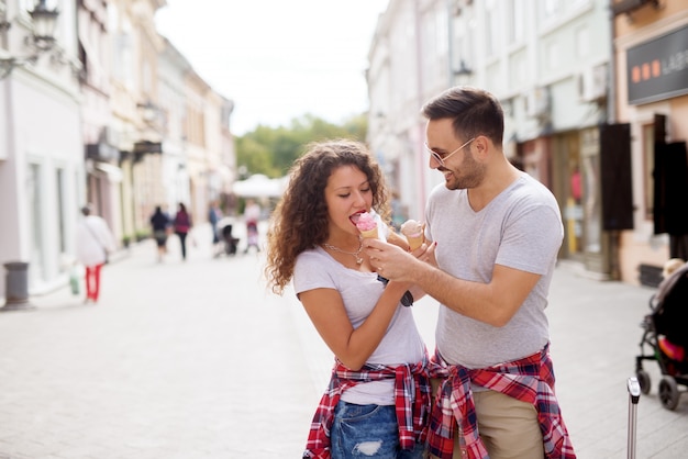 Giovane uomo affascinante sta dando il suo gelato alla sua ragazza carina per mangiare dalla sua mano in una strada.