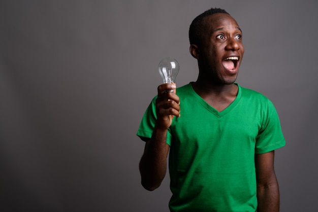 Giovane uomo africano che porta camicia verde sulla parete grigia