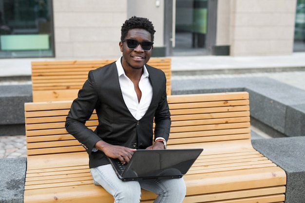 Giovane uomo africano con il portatile in panchina