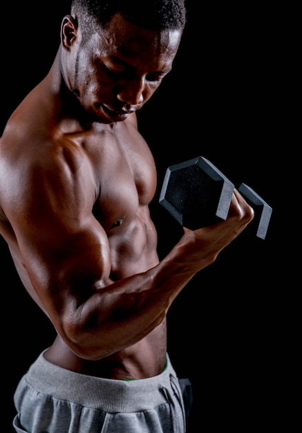 Giovane uomo africano in buona salute che si esercita con il dumbbell. Addestramento del Bodybuilder su un backgr nero