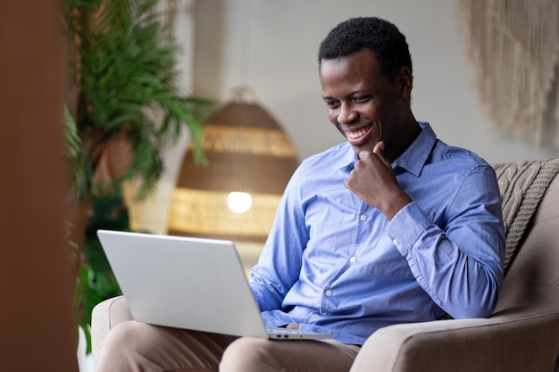 Giovane uomo africano sorridente positivo che digita sul computer portatile a casa. Lavorare da casa.