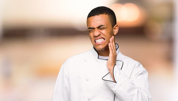 Giovane uomo afro american chef con mal di denti su sfondo sfocato