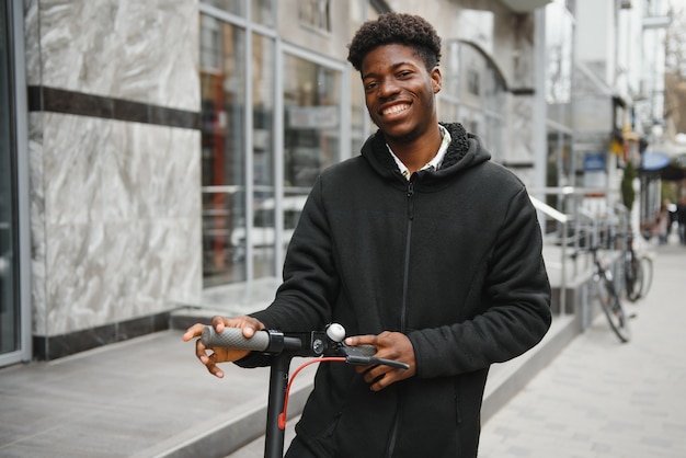 Giovane uomo afro-americano con scooter elettrico in città