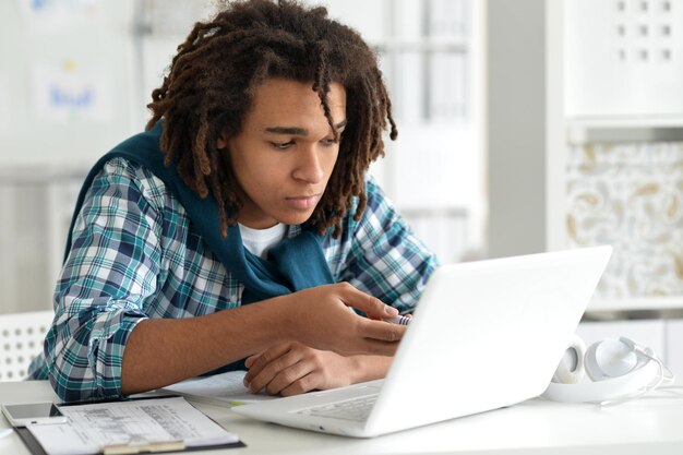 Giovane uomo afro che lavora in ufficio, usando il laptop