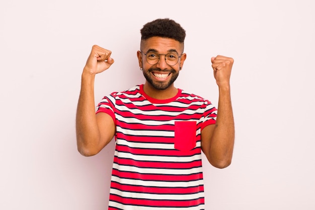 Giovane uomo afro che si sente felice, positivo e di successo che celebra i risultati della vittoria o buona fortuna