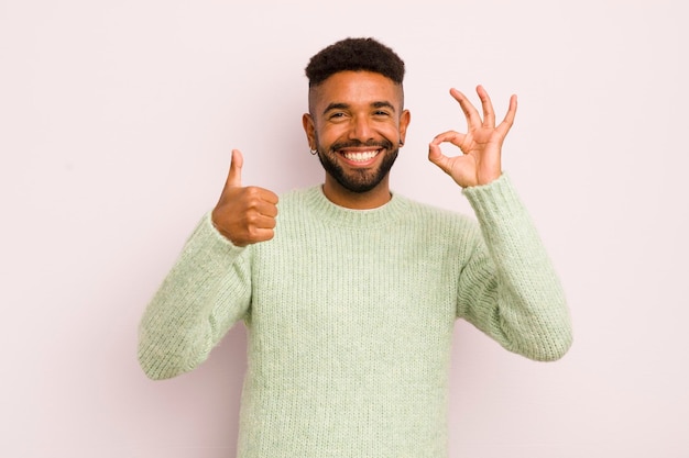 Giovane uomo afro che si sente felice stupito soddisfatto e sorpreso mostrando bene e pollice in alto gesti sorridenti