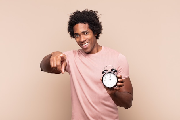 Giovane uomo afro nero che punta alla telecamera con un sorriso soddisfatto, fiducioso e amichevole, scegliendo te