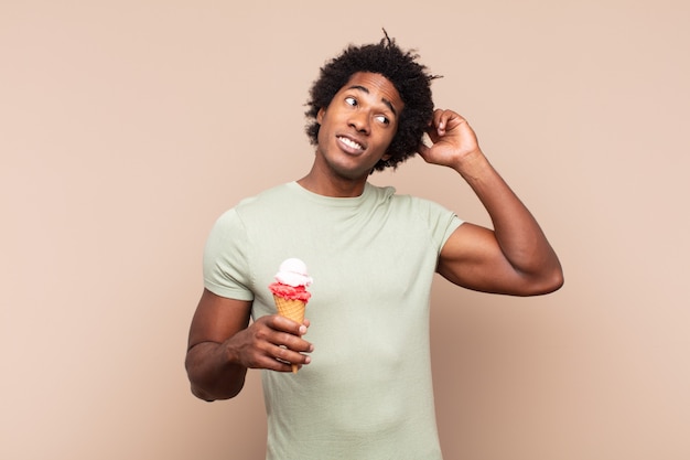 Giovane uomo afro nero che si sente perplesso e confuso, grattandosi la testa e guardando di lato