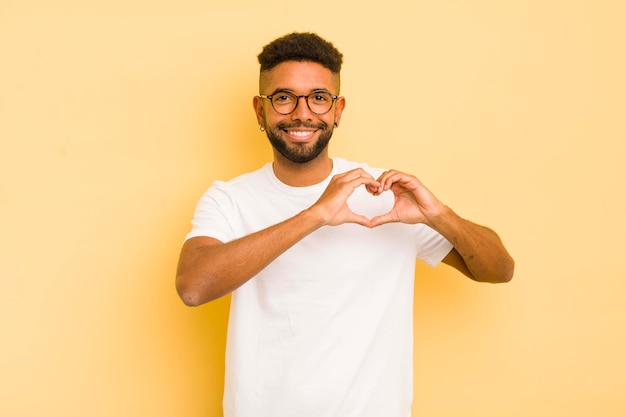 Giovane uomo afro sorridente e felice carino romantico e innamorato che fa a forma di cuore con entrambe le mani