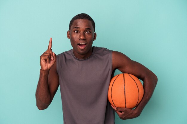 Giovane uomo afroamericano che gioca a basket isolato su sfondo blu con un'idea, un concetto di ispirazione.