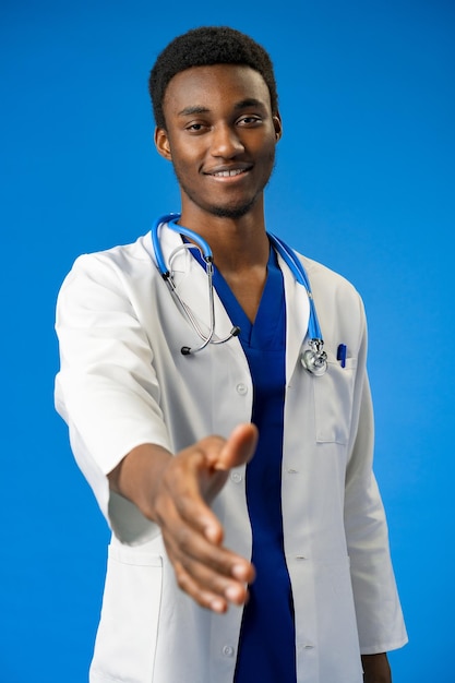 Giovane uomo afroamericano che indossa l'uniforme del medico e lo stetoscopio in studio blu