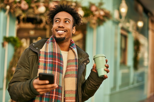Giovane uomo afroamericano che utilizza smartphone e beve caffè in città