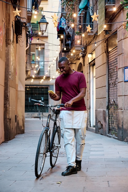 giovane uomo afroamericano con la bicicletta che cammina e usa il suo smartphone
