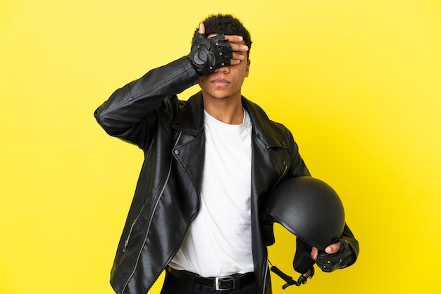 Giovane uomo afroamericano con un casco da motociclista isolato su sfondo giallo che copre gli occhi con le mani. Non voglio vedere qualcosa