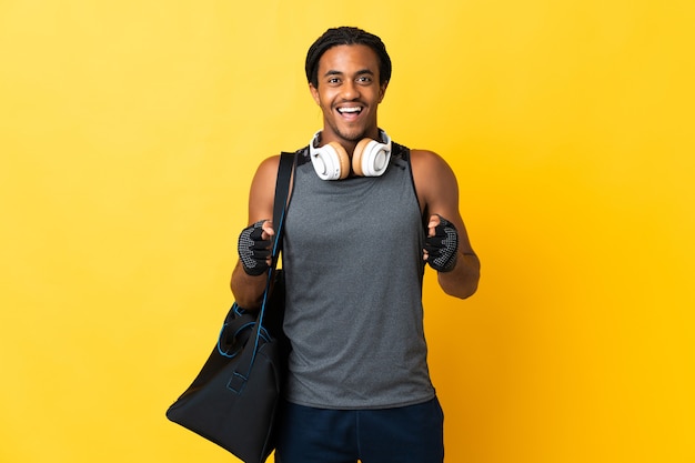 Giovane uomo afroamericano di sport con le trecce con la borsa isolata sulla parete gialla che celebra una vittoria nella posizione del vincitore