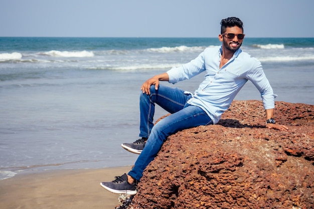 Giovane uomo afroamericano in camicia blu e jeans sulla spiaggia dell'oceano