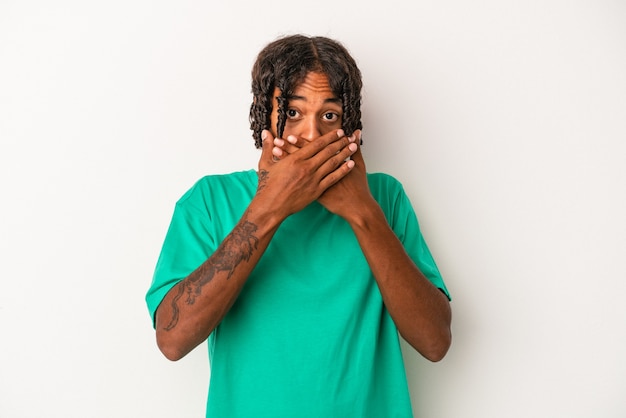 Giovane uomo afroamericano isolato su sfondo bianco che copre la bocca con le mani che sembrano preoccupate.