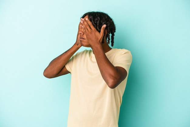 Giovane uomo afroamericano isolato su sfondo blu impaurito che copre gli occhi con le mani.