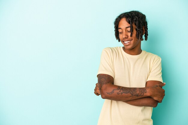 Giovane uomo afroamericano isolato su sfondo blu sorridente fiducioso con le braccia incrociate.