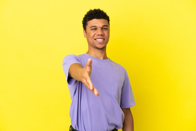 Giovane uomo afroamericano isolato su sfondo giallo che stringe la mano per aver chiuso un buon affare