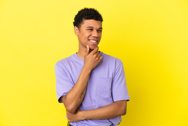 Giovane uomo afroamericano isolato su sfondo giallo guardando di lato e sorridente