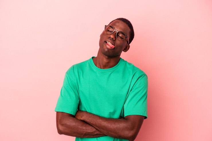 Giovane uomo afroamericano isolato su sfondo rosa divertente e amichevole che sporge lingua